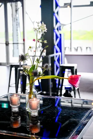 Dos velas y un arreglo floral alto blanco y verde sobre una mesa negra alta.