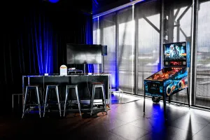 Área de videojuegos con un lounge de Nintendo Switch y sección de bar a la izquierda y una máquina de pinball a la derecha.
