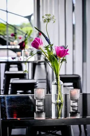 Primer plano de un arreglo floral magenta bien iluminado, en un jarrón, flanqueado por velas, sobre una mesa negra.