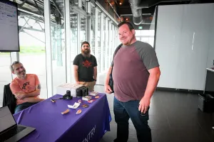 Un invitado sonriendo con representantes de Sentry en su stand de sponsor.