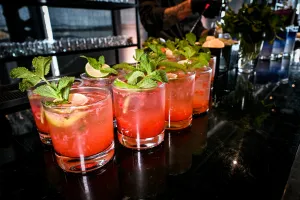 Media docena de cócteles rosas adornados con menta y limón sobre una barra negra.