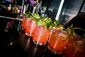 Media docena de cócteles rosas adornados con menta y limón sobre una barra negra.