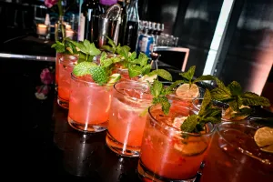 Media docena de cócteles rosas adornados con menta y limón sobre una barra negra.