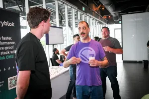 Un representante llevando una camiseta morada de Gatsby hablando con un invitado junto a los stands de sponsors.