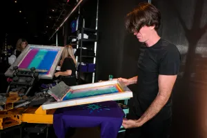 Un hombre usando la prensa de impresión de camisetas para imprimir una camiseta morada para un invitado.