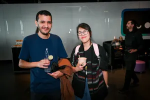Un hombre sosteniendo un cóctel morado posa con una mujer sosteniendo un aperitivo.