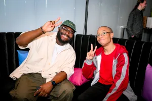 Darius, core contributor, posa en el lounge con un invitado. Ambos hombres están haciendo el signo de paz.