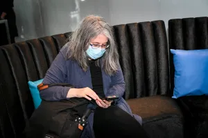 Una mujer con máscara, mirando su teléfono, mientras está sentada en el Houston lounge.