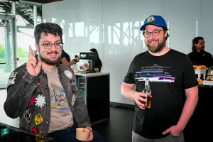 Dos invitados masculinos con gafas sonríen y posan juntos con su comida y bebida.