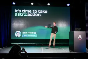 Ben Holmes en el escenario gesticulando hacia la diapositiva detrás de él que dice, "It is time to take astro:action."