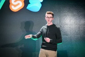 Un primer plano de Ben Holmes en el escenario frente a una diapositiva que muestra logos de otros frameworks.
