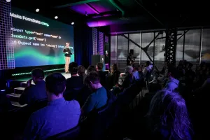 Una toma desde el lado del público. Ben Holmes está en el escenario frente a un code snippet que muestra un formulario. La diapositiva dice, "Make FormData easy."