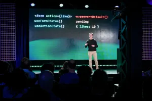 Ben Holmes en el escenario frente a una diapositiva que muestra código para un formulario con un botón like.