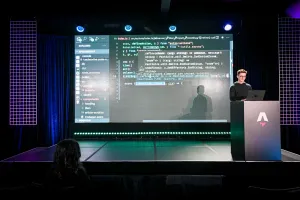 Ben Holmes en el escenario en el podio, compartiendo un demo. Está live-coding.