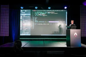Ben Holmes en el escenario en el podio, compartiendo un demo. Está live-coding.
