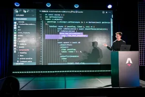 Ben Holmes en el escenario en el podio, compartiendo un demo. Está live-coding.