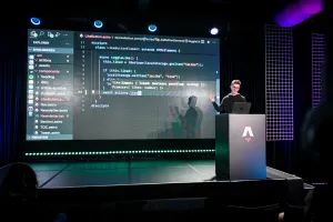Ben Holmes hablando desde un podio de marca Astro. Su mano señala un code example de un componente de botón like