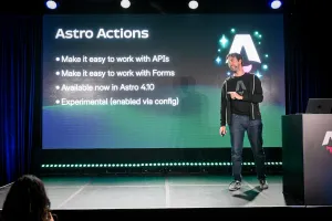 Fred K. Schott hablando en el escenario, señalando fuera del escenario al público. Detrás de él hay un resumen de Astro Actions en la pantalla LED.
