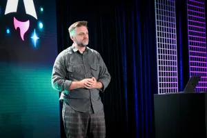 Matthew Phillips hablando en el escenario junto a un podio con un portátil encima. Detrás de él está el logo de Astro Together en pantalla.