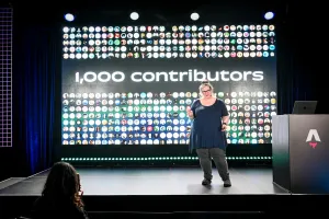Sarah Rainsberger hablando desde el lado derecho del escenario, hablando sobre cómo Docs ha tenido 1.000 contributors hasta la fecha.