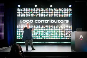 Sarah Rainsberger hablando desde el lado izquierdo del escenario, hablando sobre cómo Docs ha tenido 1.000 contributors hasta la fecha.
