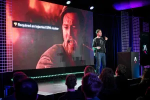 Fred K. Schott hablando en el escenario junto a un podio de marca Astro. Hay un meme de Star Wars en pantalla sobre requerir un injected SPA router.