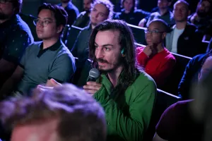 Un miembro del público sosteniendo un micrófono, preguntando a los oradores de la keynote una pregunta.