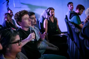 Un miembro del público sosteniendo un micrófono, preguntando a los oradores de la keynote una pregunta. Se puede ver a un miembro del equipo A/V observando atentamente al miembro del público.