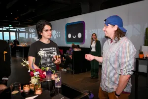Dos invitados charlan en una mesa alta con sus bebidas. Al fondo, se puede ver el Houston lounge.