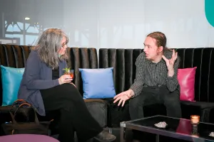Reuben, de Astro, sentado en el Houston lounge charlando con una invitada mientras ella sostiene su bebida.