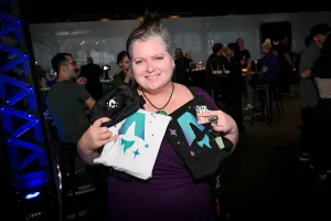 Una invitada sostiene sus camisetas impresas con el logo de Astro en blanco y negro junto con una riñonera negra con la marca del logo de Astro en blanco.