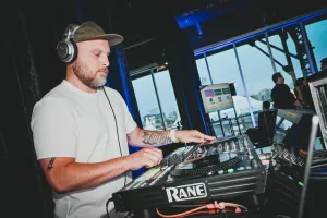 Un DJ lleva una gorra y auriculares mientras mezcla en su cabina.