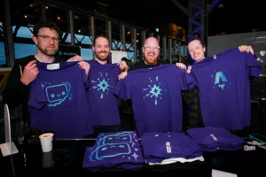 Miembros del equipo de Astro sosteniendo sus camisetas impresas púrpura de Astro. De izquierda a derecha: Matt Kane (Houston), Ema Stoppa (logo de Starlight), Nate (logo de Starlight ), y Chris Swithinbank (logo de Astro).