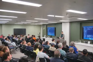 Alex haciendo una demo en vivo en el escenario frente a varias filas de asistentes.